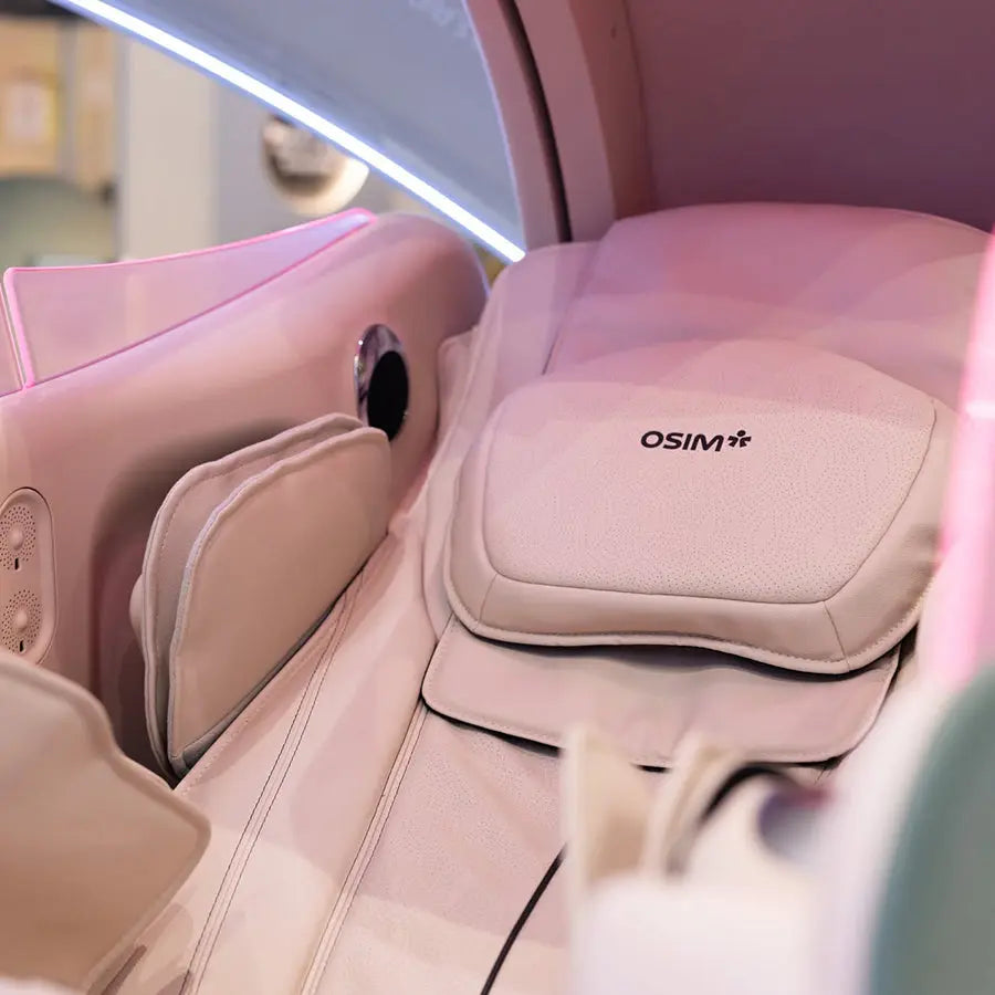 A close-up of a premium OSIM uDream·AI massage chair interior, showing the headrest cushion with the OSIM logo, side massage armrests, and ambient pink lighting.