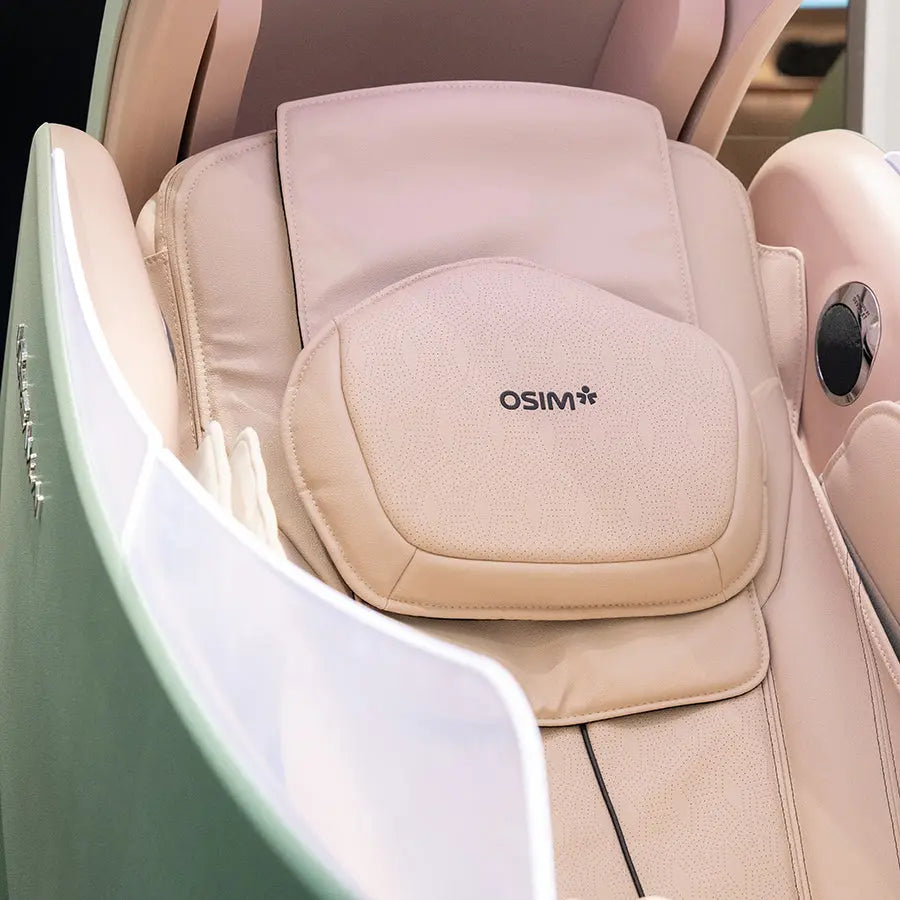 A beige padded lumbar support pillow with the brand name OSIM embroidered in black, shown installed on a matching beige massage chair.