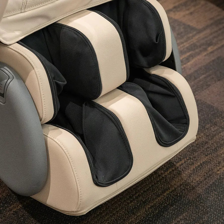 Close-up of a massage chair with cream and black padded sections, shown on a brown carpeted floor.