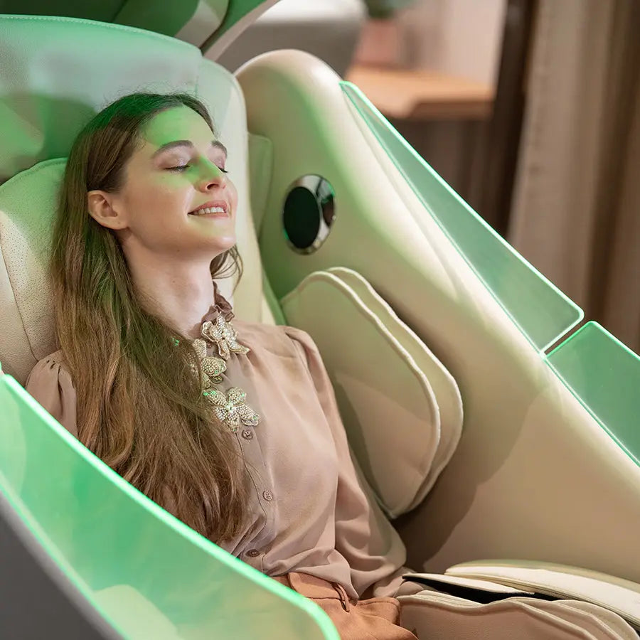 A woman reclining comfortably in a modern, light green and beige massage chair, with soft ambient lighting and a blurred indoor background.