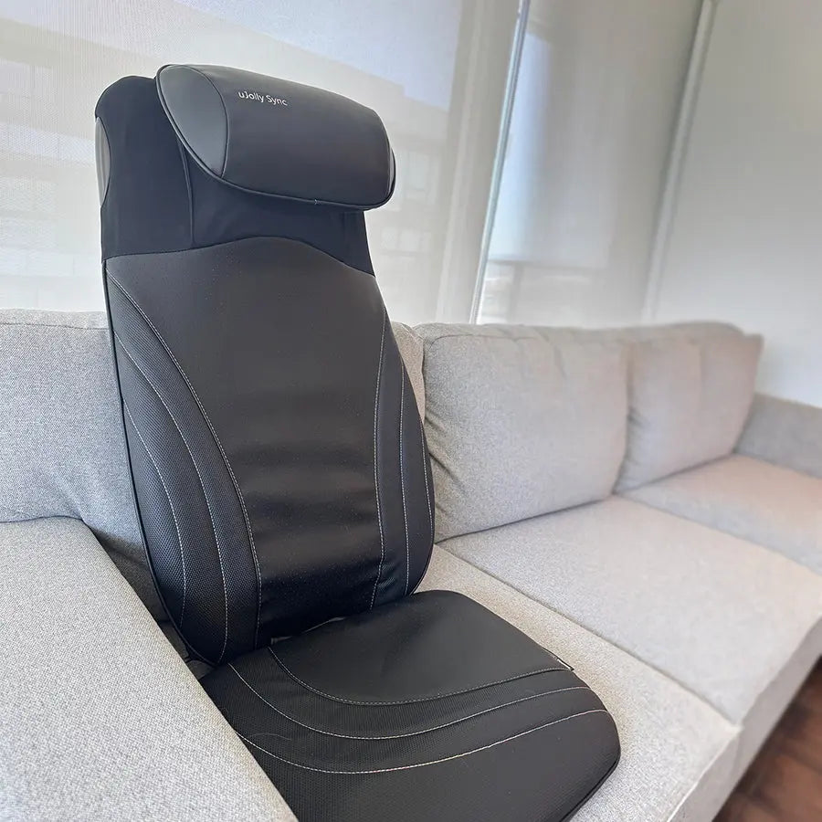 A black OSIM back massage pad massager  shown sitting on a light gray fabric sofa in a home setting.
