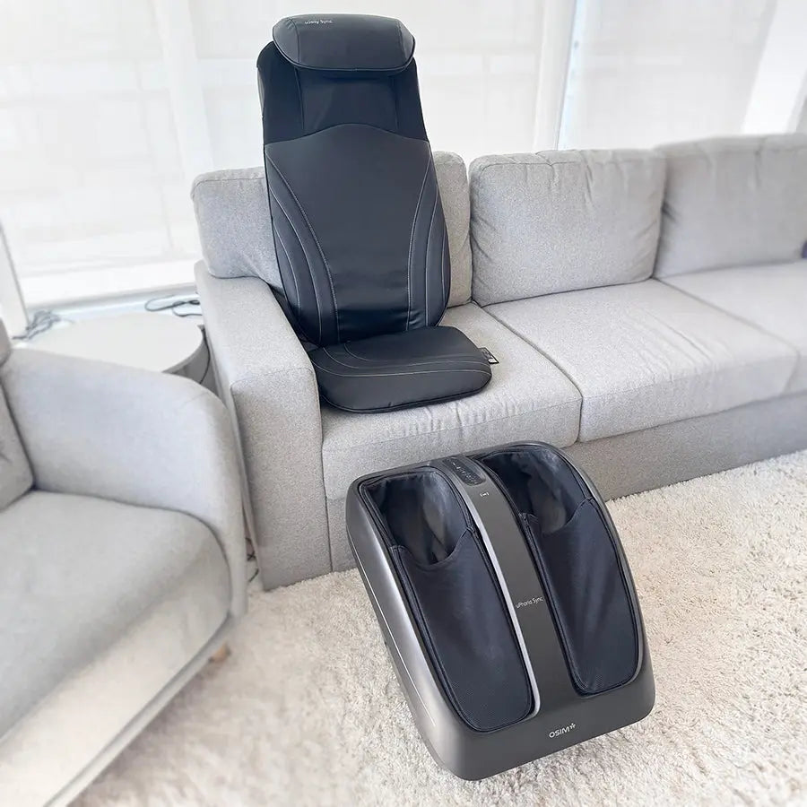 Portable black OSIM back massager and foot massager set placed on a light gray sofa and white rug in a living room setting.